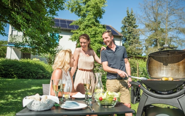 Freunde beim Grillen vor Haus mit PV-Anlage auf dem Dach
