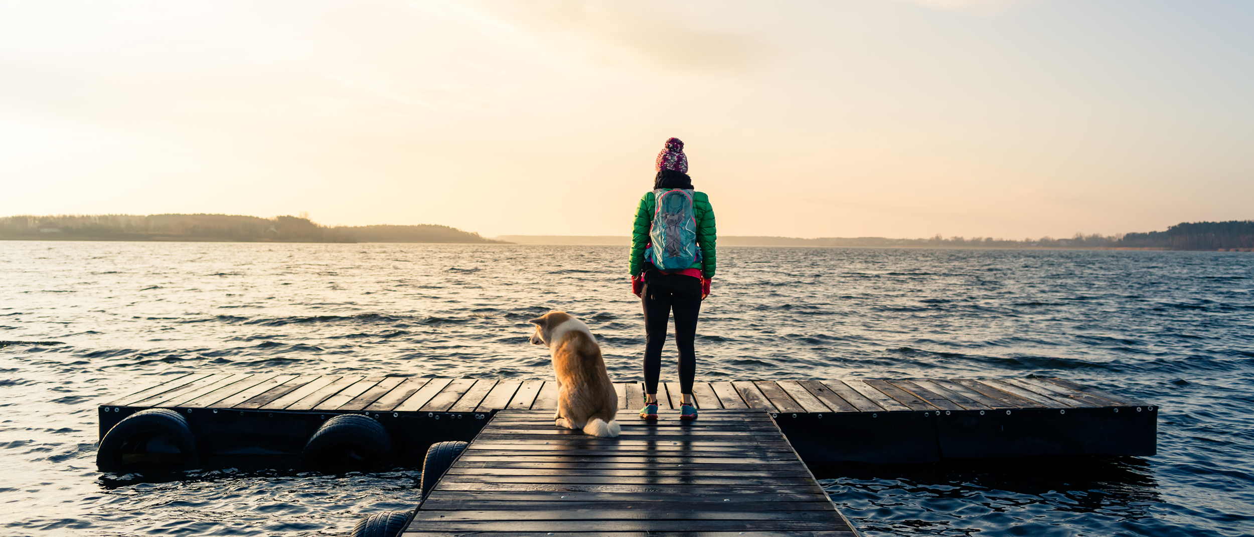 Frau und Hund genießen Sonnenaufgang auf Steg