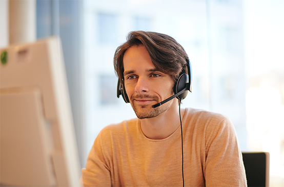 Junger Mann sitzt mit Headset auf dem Kopf am Computer
